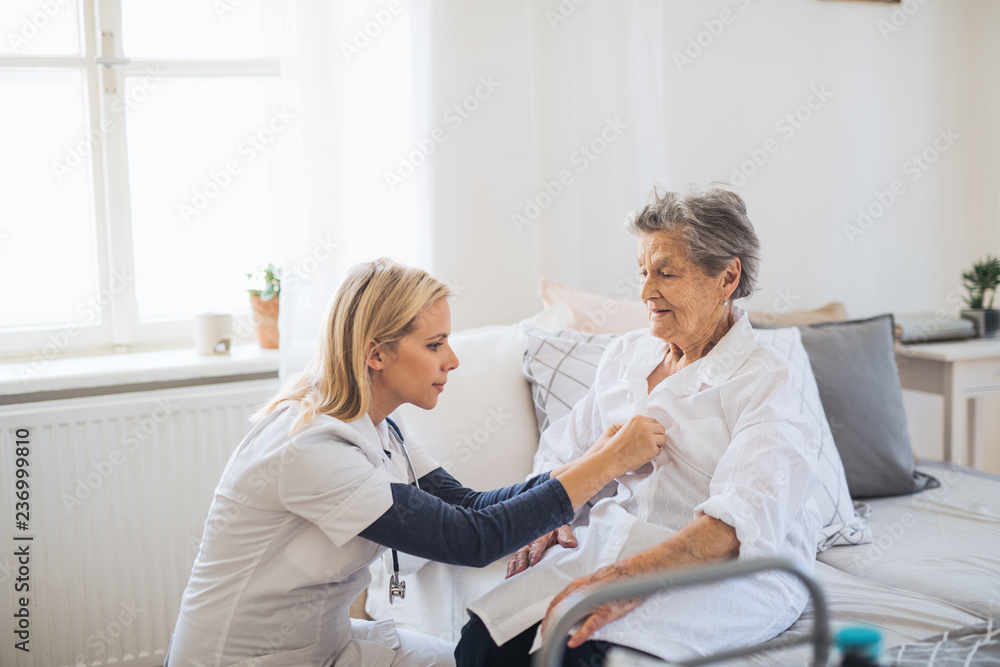 Wall mural A health visitor helping a sick senior woman sitting on bed at home.