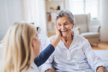 A health visitor talking to a sick senior woman sitting on bed at home. - obrazy, fototapety, plakaty