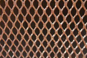 Close-up of steel grill. Steel is rusted. Focus is on top of image, diminishing moving down. Sunlight is shining on grill.