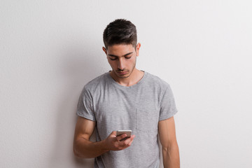 Obraz premium Young hispanic man with smartphone standing in a studio, text messaging.