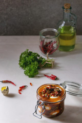Opened Jar with homemade pickled marinated quail eggs in tomato and olive oil sauce with anchovies and fresh parsley on white marble kitchen table. Ingredients above.