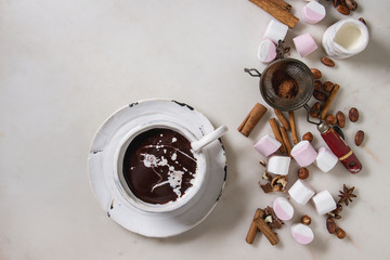 Ceramic cup of hot chocolate with marshmallow s'mores with ingredients above over white marble table. Winter drink. Flat lay, space
