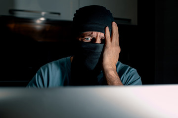 Masked hacker thoughtfully looking at the monitor 