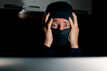Masked hacker holds his head by two hands and looking at the monitor. Epic fail.  
