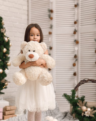 child girl playing with teddy bear near the Christmas tree