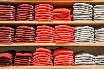 Clothes displayed in store. Copy spase for text. Lot warm sweaters of bright color are neatly stacked in a row on the store shelves. Piles of multicolored knitted woolen clothing. T-shirt on shelve