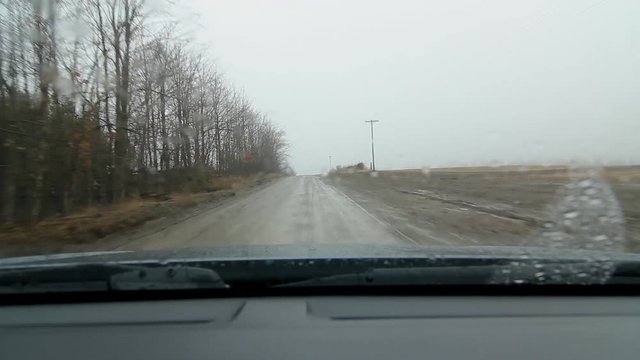 Driving on wet, muddy road next to farmers field. Rain falling. Driving north on Blezard Line approaching Division Road in Indian River, Ontario.