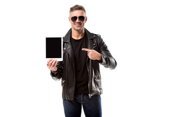 smiling man in leather jacket pointing with finger at digital tablet with blank screen isolated on white