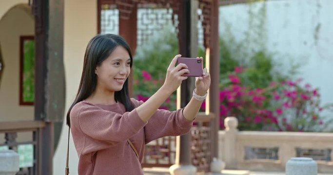 Woman take photo on cellphone inside chinese garden