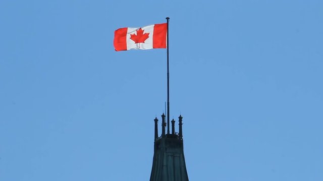 Canadian flag blowing on top of the Peace Tower, the highest point of the Parliament buildings in Ottawa, Canada. Bright blue sky background.