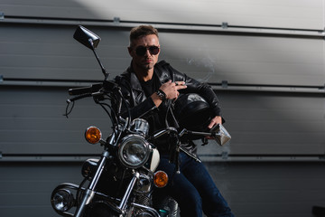 Obraz na płótnie Canvas handsome guy in black sunglasses and leather jacket sitting on motorcycle in garage