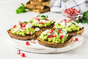 Avocado feta pomegranate toasts on cutting board. Selective focus, space for text.