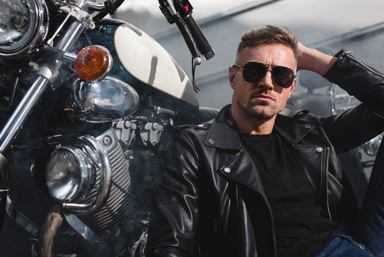 handsome guy in sunglasses sitting by motorcycle in garage