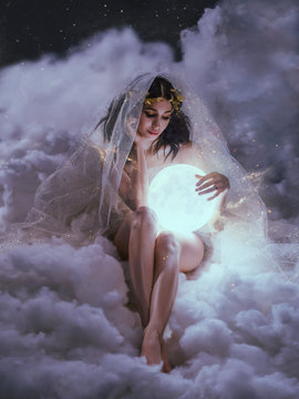 gorgeous slender sexy lady sits in the clouds and holds the moon in her hands. daughter of the sun and sky, keeper of dreams, ready to do good and a fairy tale under the cover of night and the stars