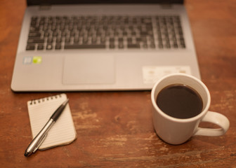Brown wooden table with laptop notepad pen and a mug of black coffee in an relaxing break time scene