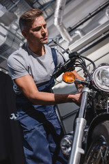 Fototapeta na wymiar handsome adult mechanic in overalls fixing motorcycle in garage