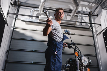 mechanic holding wrench and fixing motorbike in garage