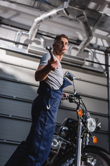 mechanic with wrench in hand next to motorbike in garage