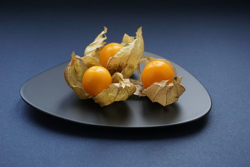 drei orangene Physalis auf schwarzen Designteller