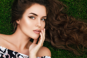 Beautiful woman with a healthy curly hair is lying on the grass