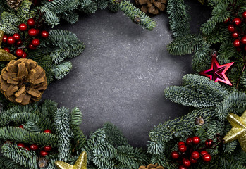 Fototapeta na wymiar Christmas frame made of fir-tree branches, festive decorations, and cones on the gray background