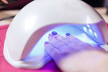 Manicured nails in UV lamp. Rays cure gel polish. professional nail art and manicure salon