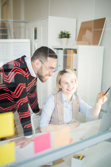 Fototapeta premium Positive excited young colleagues in casual outfits discussing marketing project in office: pretty lady pointing at monitor while explaining information to man