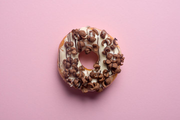 Fresh chocolate donut or doughnut decorated wit chocolate cereal on pink pastel table top