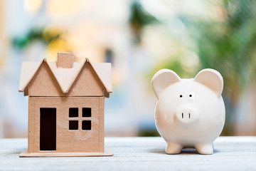 Piggy bank and model house on a bright interior room background