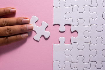 Close up of hand placing the last jigsaw puzzle piece on pink background. Business and team work concept.