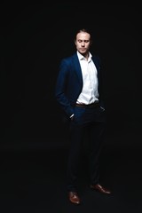 Full length of elegant young handsome man posing in fashionable suit, looking at camera. Studio shot