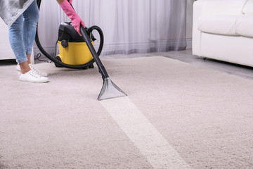 Woman removing dirt from carpet with vacuum cleaner in room