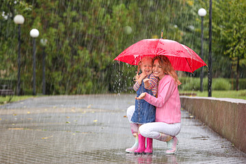 Happy mother and daughter with red umbrella in park on rainy day. Space for text