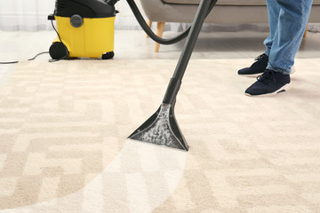 Man removing dirt from carpet with vacuum cleaner in room