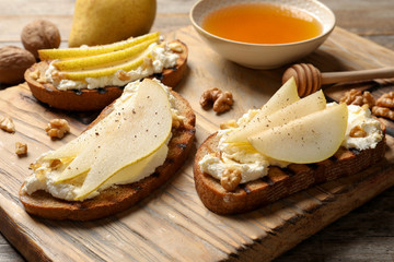 Toasted bread with tasty cream cheese and pear on wooden board