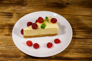 Piece of tasty New York cheesecake with raspberries in a white plate on wooden table