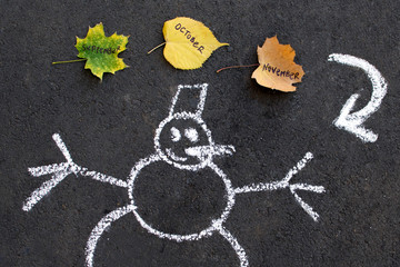 Chalk Drawing snowman on black asphalt. brown, green, yellow leaves trees with the inscription word...