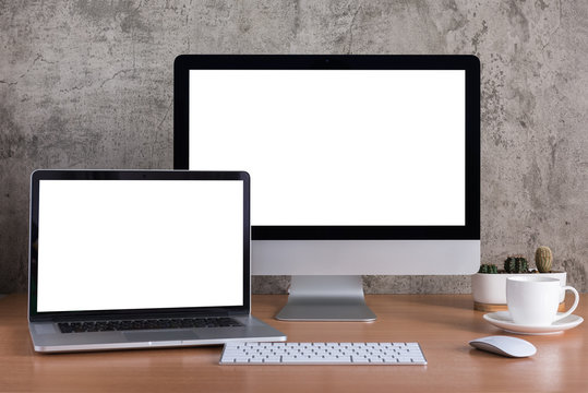 Blank screen of all in one computer and laptop computer with coffee cup and cactus vase on raw concrete background