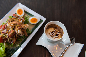Cappuccino coffee with Wing Bean Shrimp Salad on dark wooden table