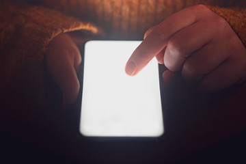 Woman using mobile smart phone at night with dramatic lighting and shallow depth of field. Blank screen with bright lighting for design mockups.