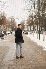 A young man turning around leaves in the city view in the city goes along the avenue. hipster man in winter city