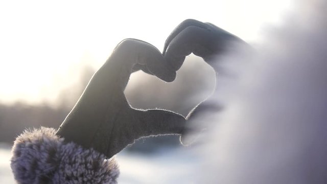 Female hands in winter gloves making a heart shape gesture while holding a solar flare.