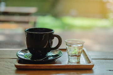 Fototapeta na wymiar Hot coffee in black cup with short water glass placed on wood tray in coffee shop