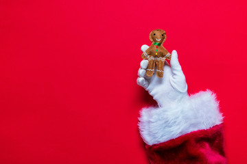 Santa Claus Christmas hand holding a gingerbread decoration against a red background