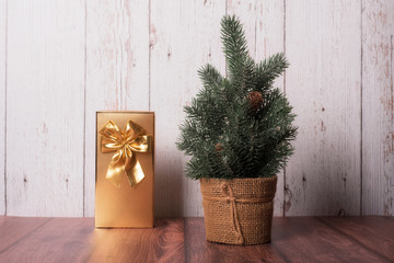 Pine tree with golden gift box on wooden background