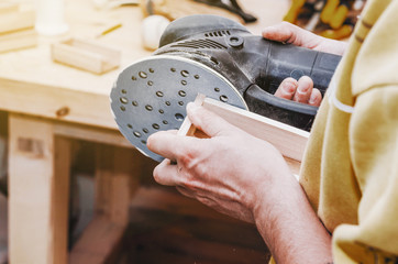 Hands a man polishes a wooden part with a grinding machine. Carpentry production. Working with wood