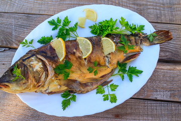 Baked carp fish with lemon and parsley on wooden table