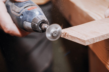 hands of a man holding a Dremel tool with an installed small circular saw. Wood processing....