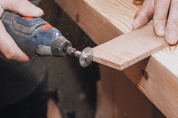 hands of a man holding a Dremel tool with an installed small circular saw. Wood processing. Workshop. Manufacture of wooden products. Joiner's cutting tool