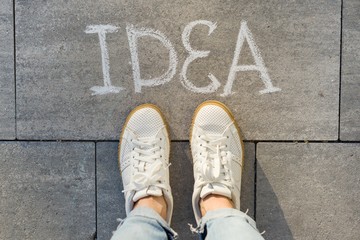 View from above, female feet with text idea written on grey sidewalk